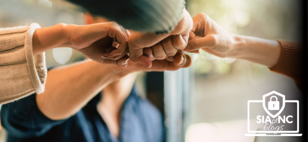 A close-up of several hands engaged in a fist bump, symbolizing teamwork and collaboration. The background is softly blurred, creating a warm, inviting atmosphere that emphasizes the connection between the individuals.